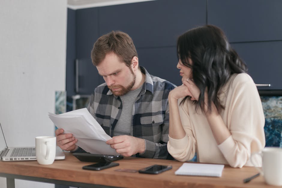 A focused couple sitting at a desk reviewing important documents in a home office setting.